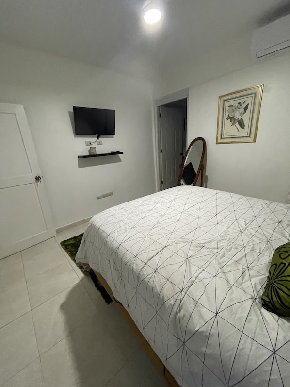 Une chambre à coucher avec un lit, un téléviseur fixé au mur, une porte et un tableau encadré.