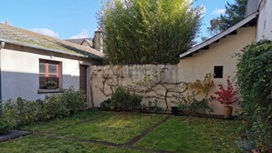 A small, enclosed garden area with a concrete wall, potted plants, and a grassy lawn. - Ô calme - 100m² apartment 15 min from Orléans (Olivet)