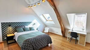 A bedroom with a sloped ceiling, a bed with patterned bedding, a desk with a chair, and a window with a view. - Ô calme - 100m² apartment 15 min from Orléans (Olivet)