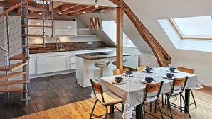 A modern kitchen with a central island, a dining area with a table set for four, and a spiral staircase leading to an upper level. - Ô calme - 100m² apartment 15 min from Orléans (Olivet)