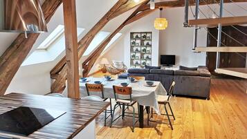 Un espace de vie de style loft avec des poutres en bois apparentes, un coin repas avec une table et des chaises, et un coin salon avec un canapé.