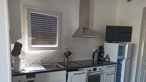 Una cocina moderna con armarios blancos, encimera negra, horno empotrado, fregadero y ventana con persianas.