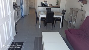 Un espacio habitable compacto con kitchenette, comedor y zona de estar con sofá y mesa de centro.