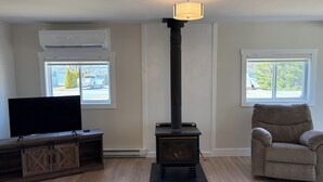 A living room with a wood-burning stove, a television on a wooden cabinet, and a chair.