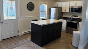 A kitchen with a central island, white cabinets, stainless steel appliances, and a wall clock.