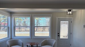 A room with two armchairs, a small table, large windows, a door with a glass panel, and a light fixture.