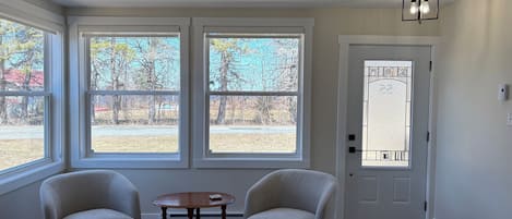 A room with two armchairs, a small table, large windows, a door with a glass panel, and a light fixture.