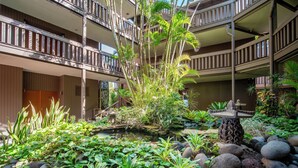 Un hôtel à plusieurs étages doté de balcons, d’un jardin central agrémenté d’un élément aquatique et de plantes tropicales.