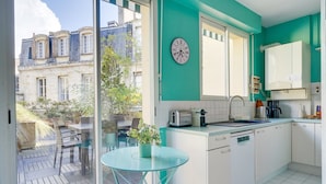 A modern kitchen with a glass table, white cabinets, and a view of a courtyard with outdoor seating. - Lovely  apartment with exceptional terrace (Bordeaux)