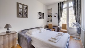 A hotel room with a bed, a desk, a chair, a lamp, and a window with curtains. - Lovely  apartment with exceptional terrace (Bordeaux)