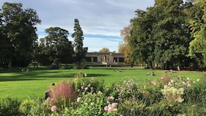 A large, open grassy area with a building in the background, surrounded by trees and flowering plants. - Lovely  apartment with exceptional terrace (Bordeaux)