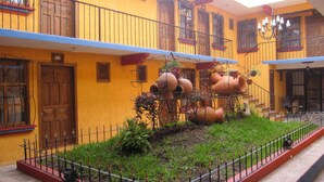 Une cour avec des pots en terre cuite posés sur un support métallique, entourée d’une clôture en métal et de verdure.