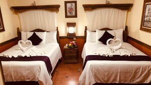 Une chambre d’hôtel avec deux lits, chacun agrémenté d’une serviette en forme de cœur et d’une petite table sur laquelle est posé un vase de fleurs.