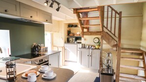 Una cocina moderna con encimera de mármol, cafetera y una escalera de madera que lleva a una zona tipo loft.