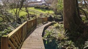 Un puente de madera en un jardín, con vista a una casa al fondo.
