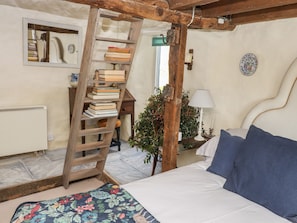A bedroom with a wooden ladder, a bed with blue pillows, a radiator, a mirror, and a wall-mounted plate.