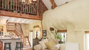 Una sala de estar acogedora con un sofá, una pequeña mesa redonda, una escalera y una zona de cocina con taburetes.