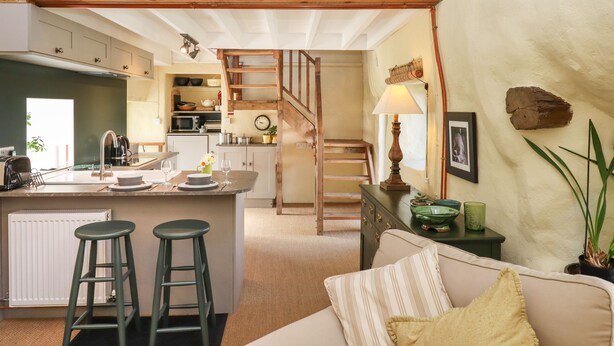 Una cocina amplia con una isla central, una escalera de madera y una zona de estar acogedora con un sofá y una lámpara.