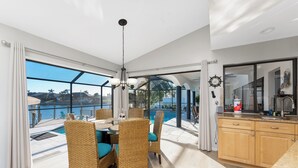 Ett rymligt rum med matplats, kök och stora fönster med utsikt över en pool.