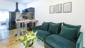 Ein modernes Wohnzimmer mit einem grünen Sofa, einem Essbereich mit einem Glastisch und einer Küche mit einer schwarzen Dunstabzugshaube.