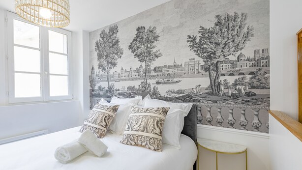 Ein Hotelzimmer mit Bett, einem großen Fenster, einem Stadtbild-Fresko und einem Kronleuchter.