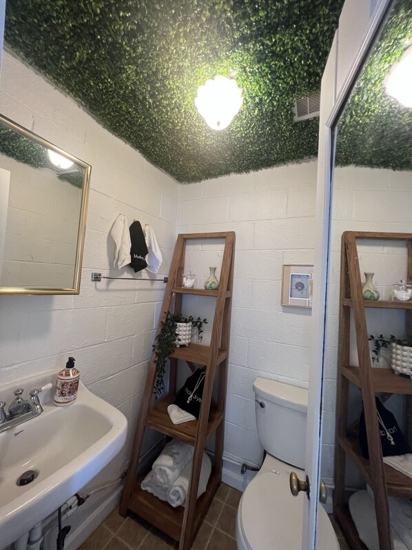 A bathroom with a white sink, wooden shelves, a toilet, and a mirror.