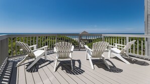A deck with three white Adirondack chairs facing a clear blue sky and ocean view. - Beautifully updated oceanfront condo with a pool (Atlantic Beach)