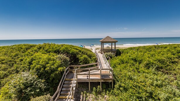 A wooden boardwalk leading to a gazebo on a beach, surrounded by dense greenery. - Beautifully updated oceanfront condo with a pool (Atlantic Beach)