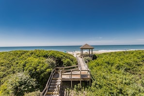 A wooden boardwalk leading to a gazebo on a beach, surrounded by dense greenery. - Beautifully updated oceanfront condo with a pool (Atlantic Beach)