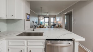 A modern kitchen with white cabinetry, a marble countertop, and a built-in dishwasher. - Beautifully updated oceanfront condo with a pool (Atlantic Beach)