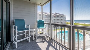 A balcony with white chairs and a view of a pool and beach. - Beautifully updated oceanfront condo with a pool (Atlantic Beach)