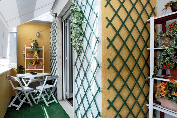 A small, enclosed balcony with a green artificial turf floor, white metal chairs, and a white table. There are potted plants on a metal shelf and a lattice wall. - Apt. near S.Peter & beautiful terrace (Roma)