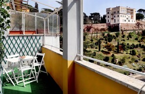 A balcony with a white table and chairs, a green mesh screen, and a view of a hillside with trees and buildings. - Apt. near S.Peter & beautiful terrace (Roma)