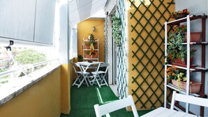 En balkon med et hvidt bord og stole, kunstgræs og plantekasser på hylder.