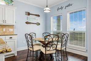 A dining area with a glass-top table surrounded by metal chairs, a white cabinet with drawers, and a wall-mounted sign that reads "Good Times". - Ocean view, backyard playset and fire pit, game room, great for kids and pets! (Crystal Beach)