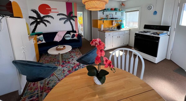 A compact kitchen with a stove, sink, and white cabinets. There's a dining area with a wooden table and blue chairs.