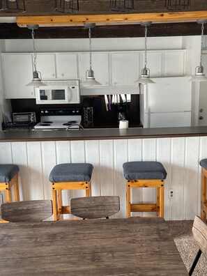 A kitchen with white cabinets, a microwave, a stove, and bar stools.