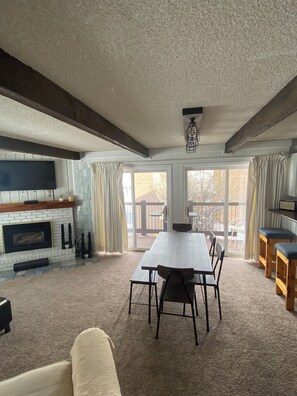 A spacious living area with a fireplace, a dining table, and a large window offering a view of the outdoors.