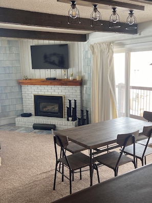 A living room with a fireplace, a flat-screen TV mounted on the wall, and a dining table with chairs.