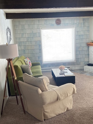 A living room with a green sofa, beige armchair, and a coffee table with books and a vase.