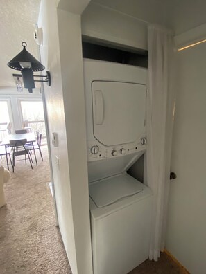 A compact room with a built-in washer and dryer, a dining area with a table and chairs, and a window providing natural light.
