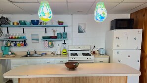 A modern kitchen with a central island, bar stools, a microwave, a refrigerator, and various kitchen appliances.