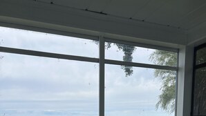 A room with a large window overlooking a grassy area and a body of water. There are two chairs with cushions and a small table.