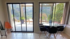 Una cocina con encimera de madera, armarios blancos y un ventanal corredero que da a un patio exterior con mesa y sillas.