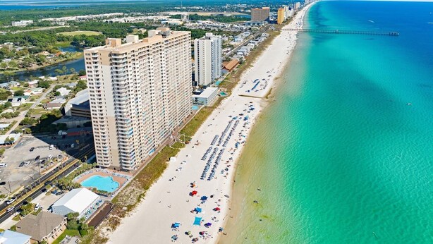 Un paisaje urbano costero con un hotel frente a la playa que cuenta con varios pisos, una piscina y una playa con sombrillas y tumbonas.