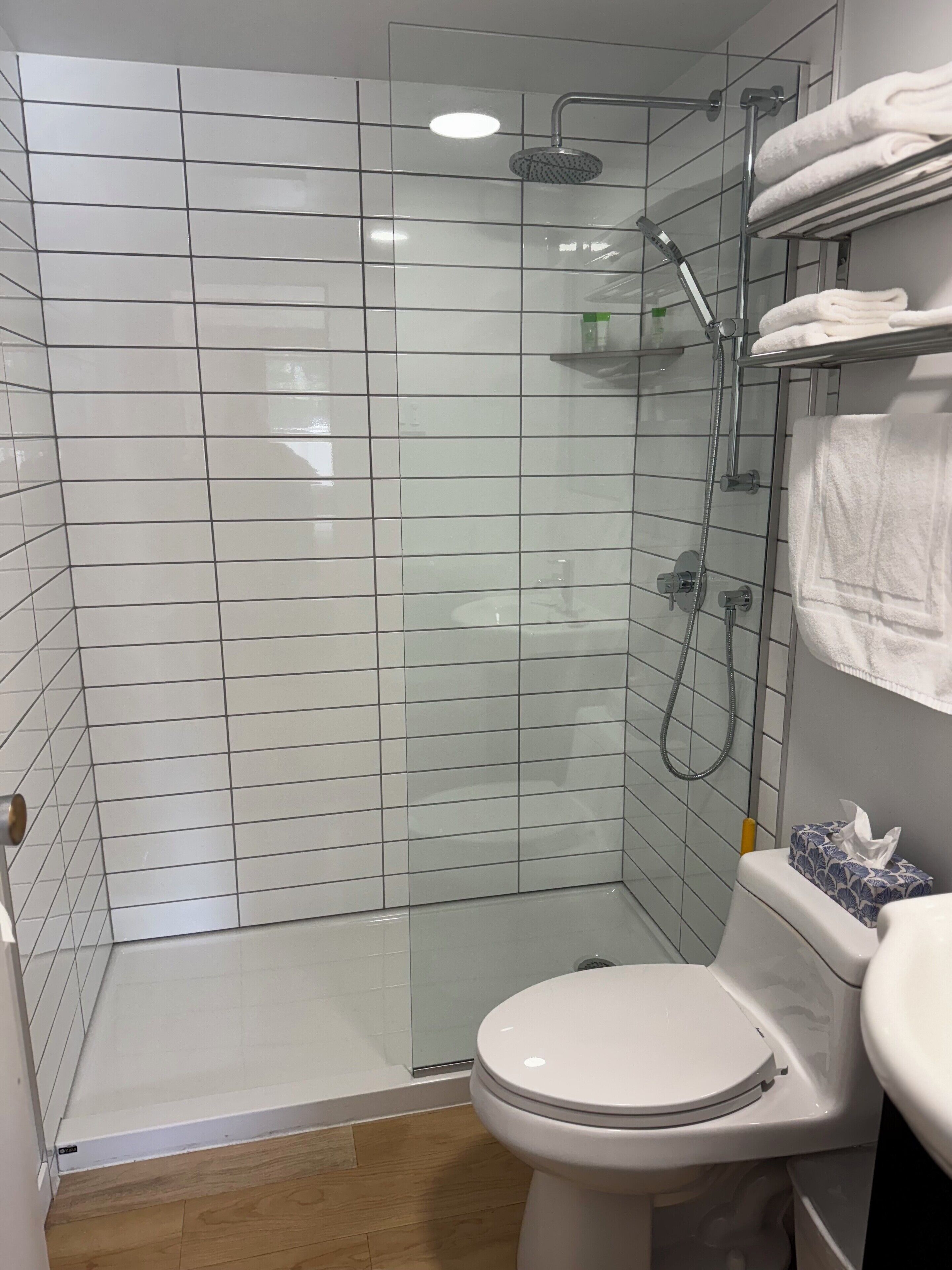 Ein modernes Badezimmer mit einer Duschkabine, einer weißen Toilette und einem Ablagefach mit gefalteten Handtüchern.