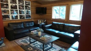 A cozy living room with two black leather sofas, a coffee table with books and a vase, and a wall of framed photos. - Kitimat Lodge (Kitimat)