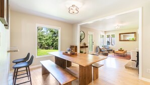 Un vaste espace de vie comprenant une table à manger en bois, des bancs et une vue sur un jardin grâce à de grandes fenêtres.