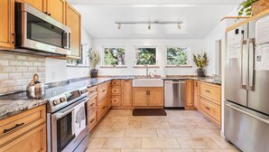 Une cuisine moderne avec des meubles en bois, des appareils électroménagers en acier inoxydable et de grandes fenêtres.
