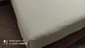 A neatly made bed with a white bedspread and pillows, a stone-textured headboard, and a wooden nightstand with a lamp. - Hotel Beraka (Ezequiel Montes)